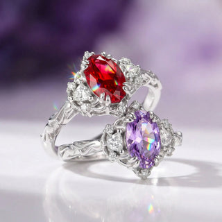 Silver ring with red and purple gemstones on a reflective surface with a blurred purple background