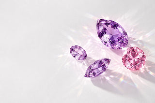 Loose purple pear, marquise and oval gemstones with a round pink stone on a white surface, Aquamarise Ethical Sourcing page mobile banner