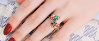 Close-up of a hand wearing a decorative ring with green gemstones on a checkered fabric background.