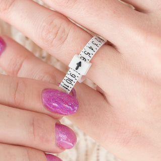 Close-up of a hand with a ring on a finger, using a measuring tape around the finger.