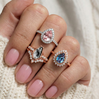 Three diamond rings with pear-shaped gemstones on a hand against a neutral background