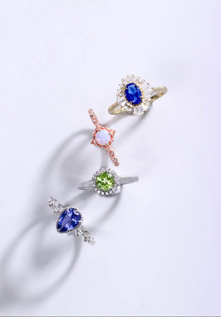 Four gemstone rings on a gradient purple background