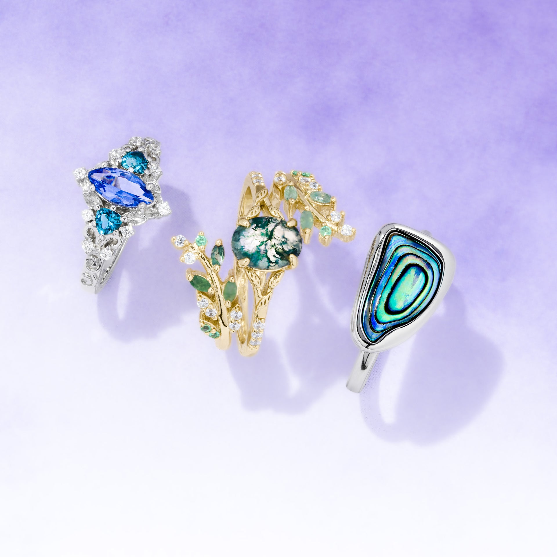 Three decorative rings with gemstones on a light purple background