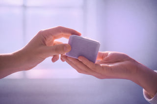 Two hands exchanging a small purple wallet against a light background