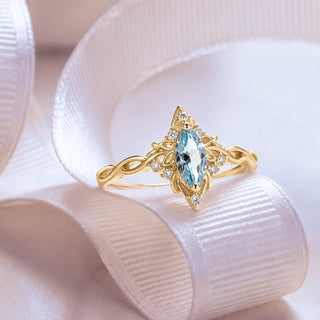 Yellow gold marquise aquamarine ring with an infinity twist band resting on a blush silk ribbon, Aquamarise collection banner