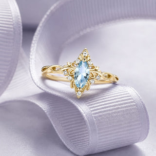Yellow gold marquise aquamarine ring with a vintage filigree halo displayed on a white silk ribbon, Aquamarise collection banner
