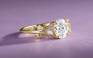 Yellow gold oval moissanite engagement ring with a nature-inspired leaf and vine band on a lilac background, Aquamarise collection banner