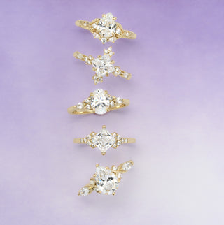 Set of five gold rings with diamond-like stones on a light purple background
