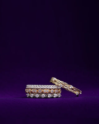 Stacked diamond eternity bands and a gold leaf ring on purple velvet
