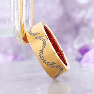 Angled view of the brushed gold titanium men's band with engraved laurel vine and crushed red garnet lining the inside