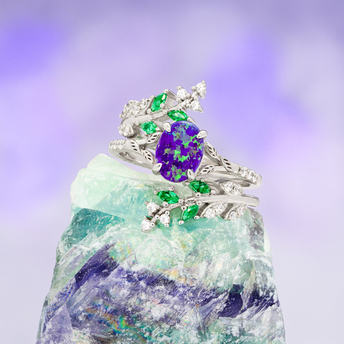 Silver ring with purple gemstone and green stones on a rock with a purple background