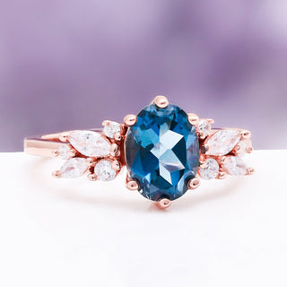 Angled view of the Lily London blue topaz ring in 14K rose gold vermeil showing the oval topaz and marquise cluster shoulders