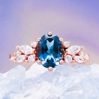 Lily London blue topaz ring in 14K rose gold vermeil resting on a white crystal, oval blue topaz with marquise cluster shoulders