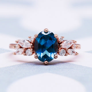 Lily London blue topaz ring in 14K rose gold vermeil on a soft white surface, oval blue topaz with a rose gold marquise cluster band