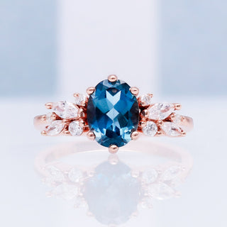Lily London blue topaz ring in 14K rose gold vermeil on a reflective white surface, oval London blue topaz with marquise accents