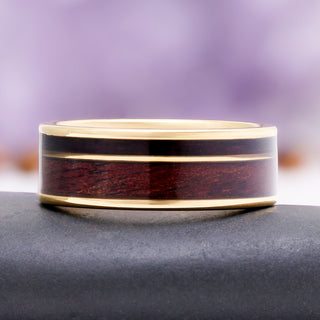 8mm M1 Garand and purpleheart wood wedding band in gold tungsten carbide resting on a dark stone