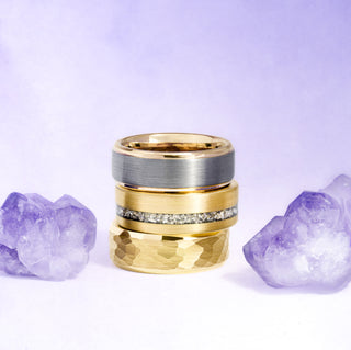 Stack of gold and silver rings with purple crystal stones on a light purple background