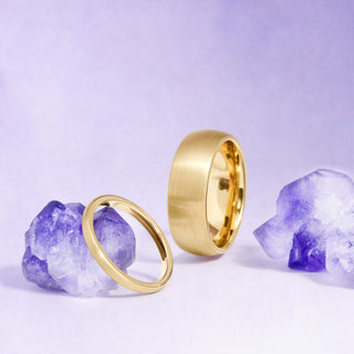 Two gold rings on purple crystal stones against a light purple background
