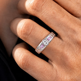 Close-up of the 6mm Moissanite & Amethyst wedding band in sterling silver worn on a hand, bezel-set oval moissanite between two amethyst pears