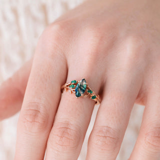 Close-up of a hand wearing a moss agate and emerald ring on a neutral background