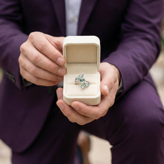 Person holding a ring in an open box, wearing a purple suit.
