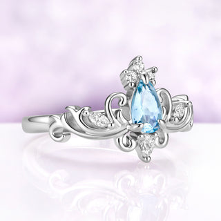 Angled view of the Odette aquamarine tiara ring showing the pear center, three-stone crown and marquise accents on the scrolled shoulders