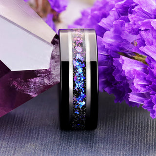 Orion Nebula fire opal men's band in black tungsten with an offset galaxy inlay and silver stripe, standing beside an amethyst crystal