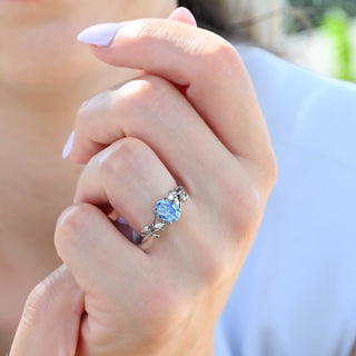 Oval cut ice blue moissanite ring with leaf band shown on the hand from a wider angle
