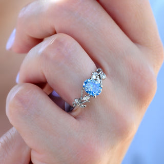Oval cut ice blue moissanite leaf ring worn on a model's hand, close-up