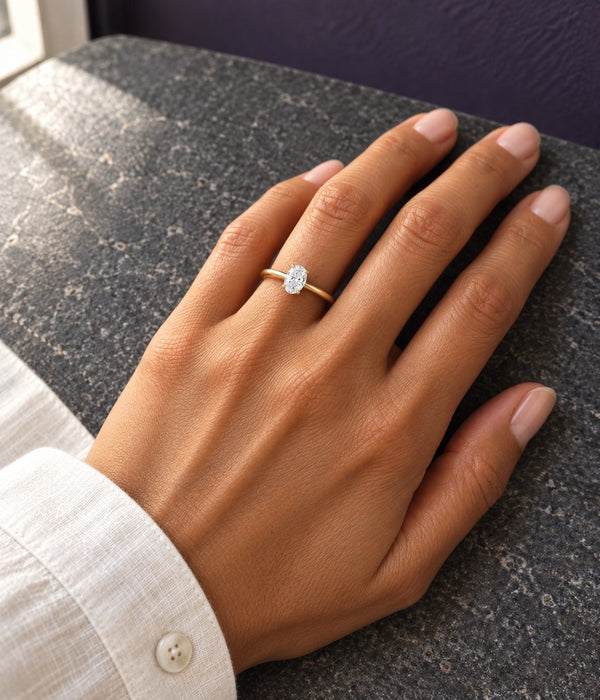 Hand resting on a grey tweed chair wearing an oval engagement ring in yellow gold, Aquamarise banner