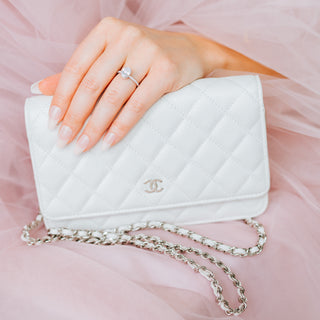 White quilted handbag with gold chain held by a hand on a pink background