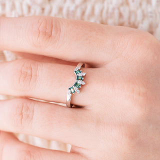 Silver ring with green gemstones on a finger against a neutral background