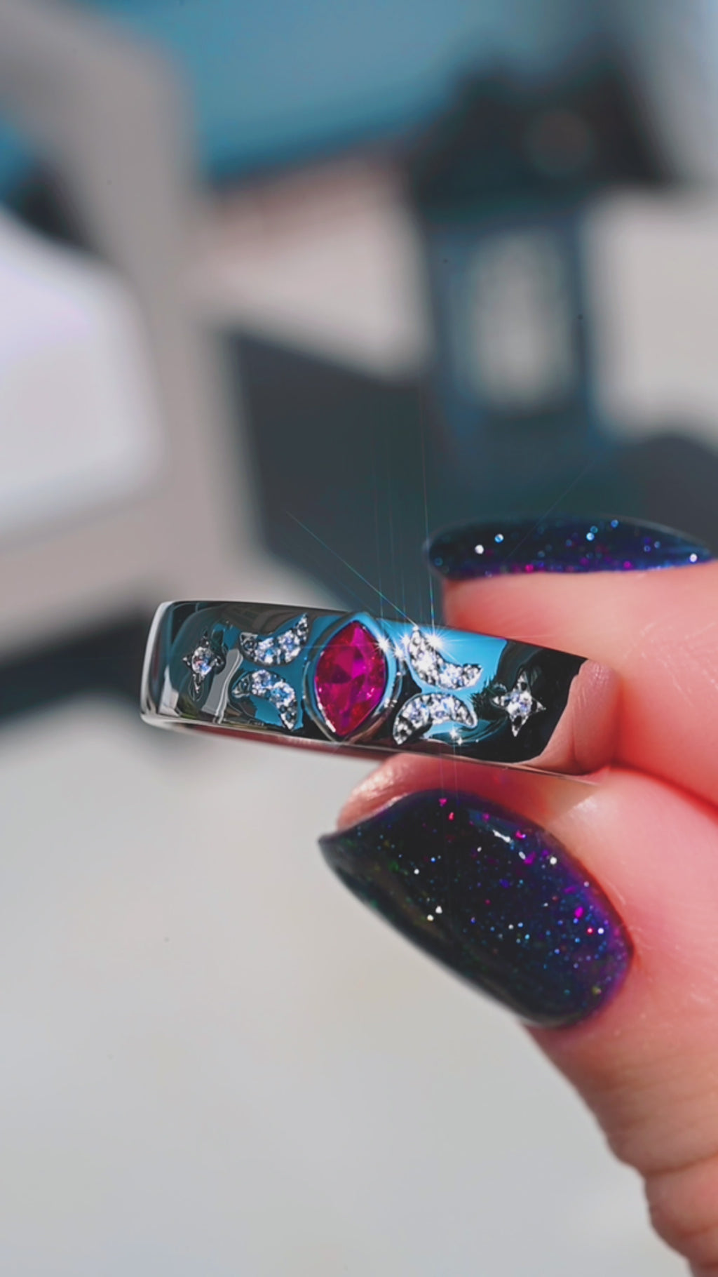 Ruby Celestial 6mm wedding band in black ruthenium held to the light, showing the bezel-set marquise ruby and pave star detailing