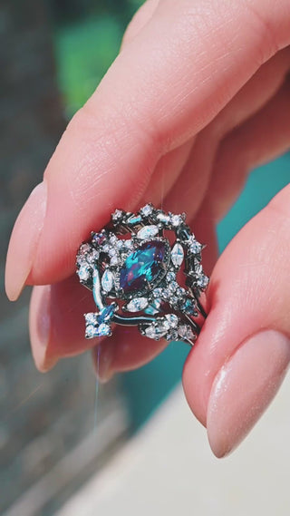 Video of the Nightbriar Lab-Grown Alexandrite Bridal Ring Set in Black Ruthenium by Aquamarise held in daylight, the engagement ring nested between its two bands