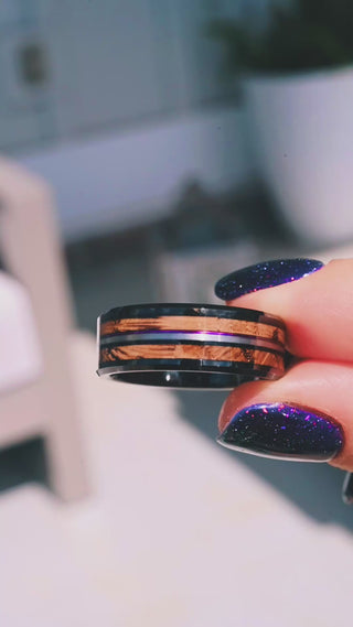 Video of the Whiskey Barrel & Purple Fishing Line Men's Wedding Band in Black Tungsten (8mm) by Aquamarise held in daylight, whiskey barrel wood inlay with a purple line