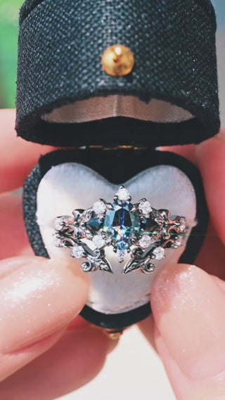 Video of the Carmilla Gray Moissanite & Black Onyx Engagement Ring in Black Ruthenium by Aquamarise, presented in a heart-shaped velvet ring box