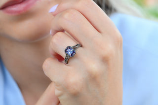 Radiant cut alexandrite engagement ring with filigree band in black ruthenium worn on a model's hand