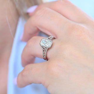 Radiant cut moissanite engagement ring with filigree band worn on a model's hand