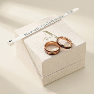 Two rose gold rings on a jewelry box with a pen and ruler.