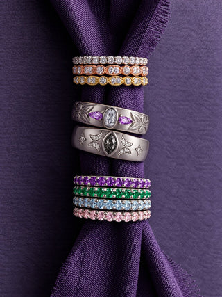 Wedding bands stacked around a gathered purple ribbon: vintage diamond bands in white, rose and yellow gold, moissanite and amethyst band, gray moissanite celestial band and minimalist amethyst, emerald, aquamarine and morganite bands, Aquamarise banner