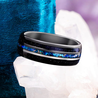 Starry Night black tungsten men's band with a center blue opal and meteorite channel, resting on a clear quartz crystal