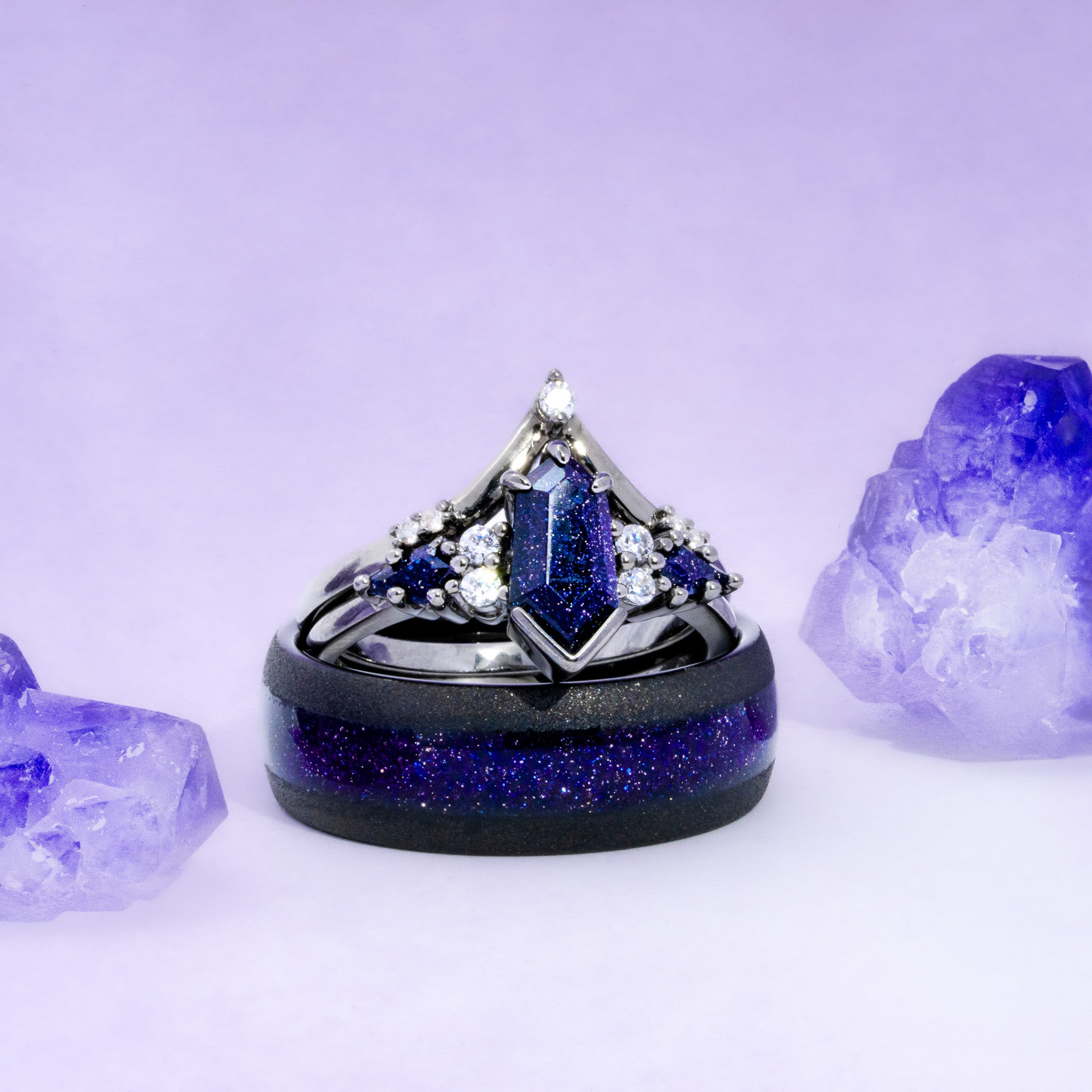 Celestial gothic couples set: a black-finish elongated hexagon blue sandstone ring with a pointed chevron band beside a black men's band inlaid with glittering blue sandstone