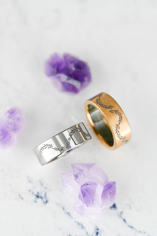 Two rings, one gold and one silver, on a marble surface with purple flowers. titanium men's wedding bands 