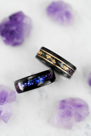 Two black rings with colorful inlay on a white surface with purple flowers. tungsten carbide men's wedding bands 