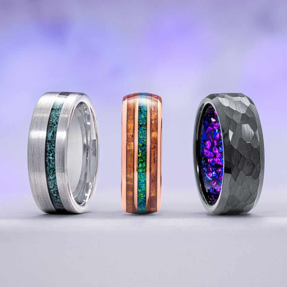 Three unique men's rings with colorful gemstone inlays on a gradient background