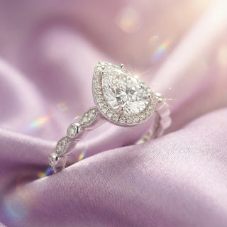 Diamond ring with a pear-shaped center stone on a soft pink fabric background