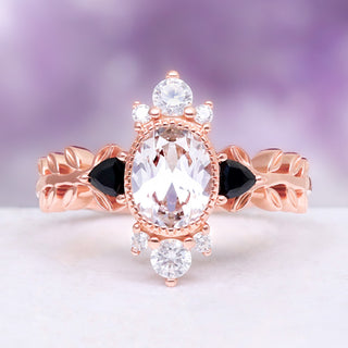 Oval lab-grown white sapphire engagement ring with trillion black onyx side stones on a carved leaf band in 14K rose gold vermeil